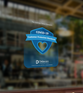 Image shows a window cling on a business that says "This business follows Delaware's COVID-19 customer protection standards."